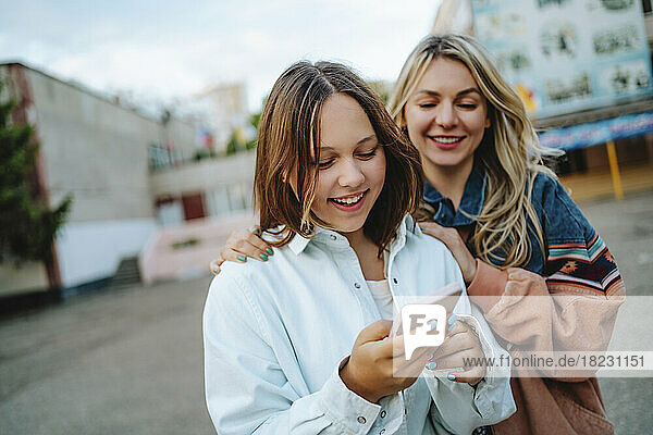 Smiling mother with daughter using mobile phone