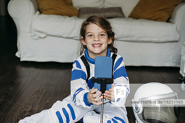 Happy girl wearing space costume with mobile phone in living room