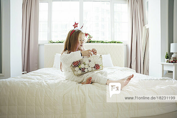 Mädchen sitzt mit einem Korb voller Weihnachtskugeln zu Hause im Bett