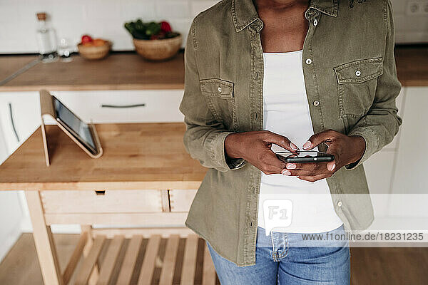 Woman using smart phone standing in kitchen at home