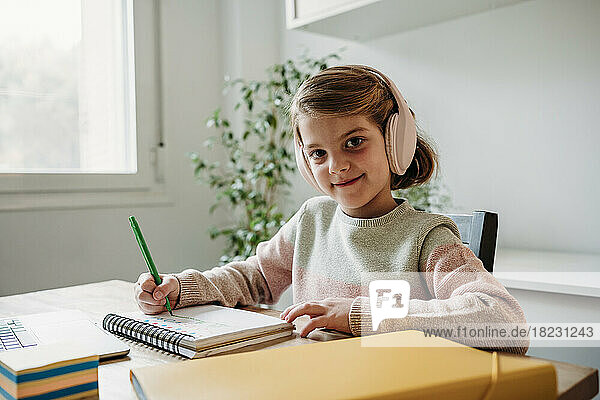 Smiling girl with wireless headphones studying at table at home