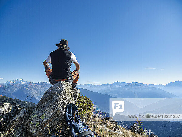 Senior man wearing hat sitting on rock in front of mountains at Vanoise national park  France