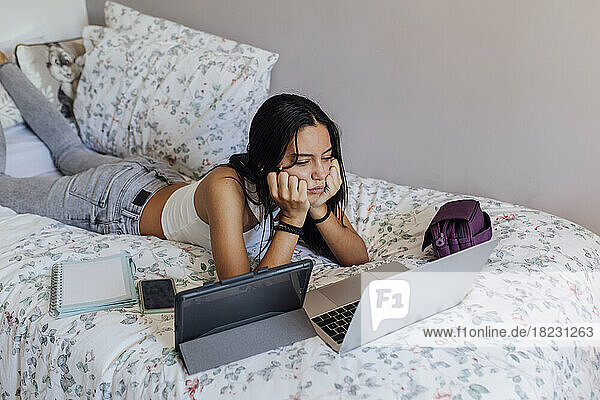Girl with head in hands watching laptop on bed at home
