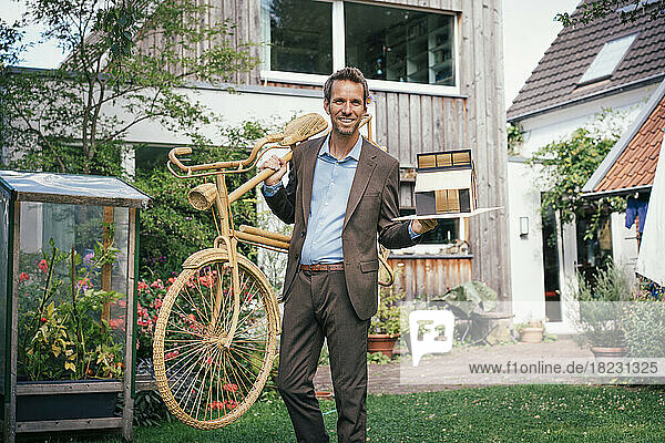 Happy real estate agent standing with bicycle and model house