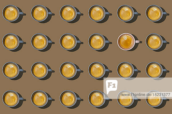 Pattern of cups of coffee standing in rows against brown background with single one looking different