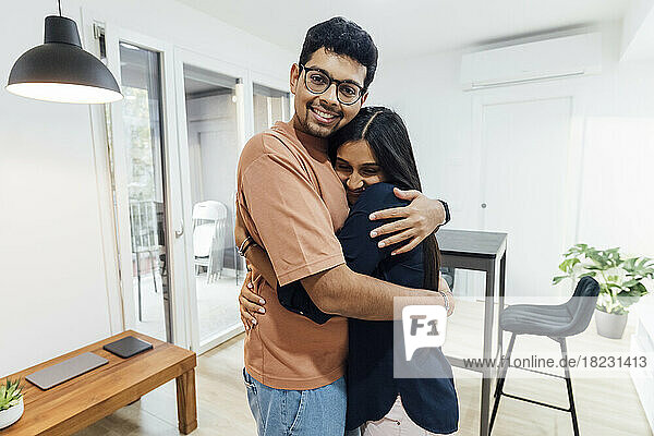 Lächelnder junger Mann umarmt glückliche Frau im heimischen Wohnzimmer