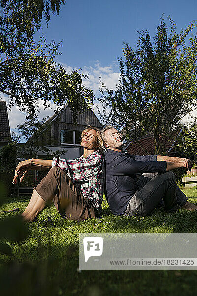 Man and woman sitting with eyes closed on grass in back yard