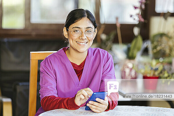 Happy young caregiver sitting with smart phone at home
