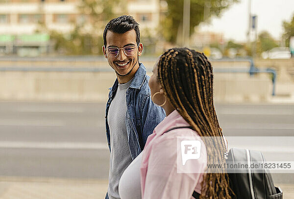 Smiling young man walking with girlfriend at footpath