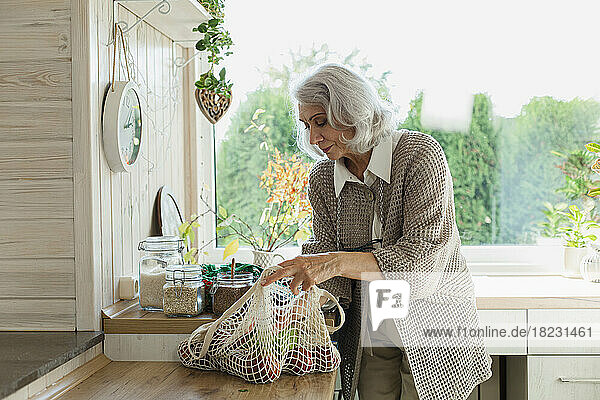 Senior woman unpacking fresh groceries in kitchen