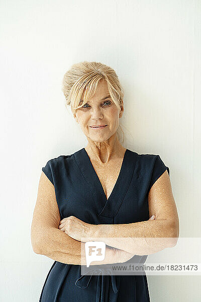 Smiling businesswoman with arms crossed in front of white wall