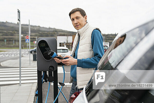 Man with smart phone and charger standing at charging station