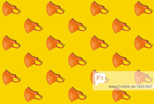 Pattern of rows of orange colored FFP2 masks flat laid against yellow background