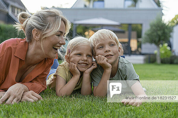 Happy mother looking at children leaning on elbows in garden