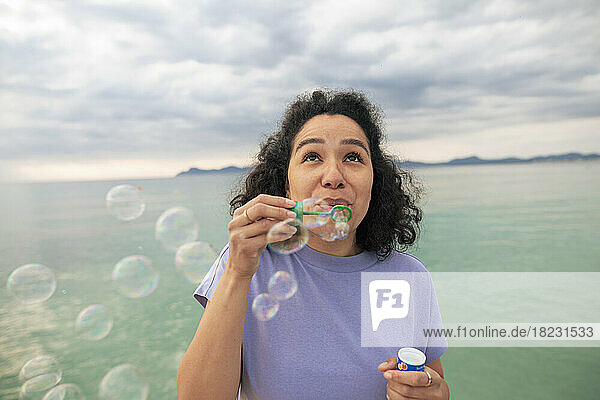Woman enjoying blowing bubbles standing in front of sea