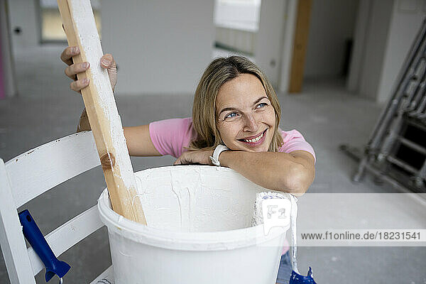 Happy woman day dreaming leaning on paint bucket in apartment