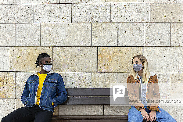 Young couple wearing protective face masks sitting on bench