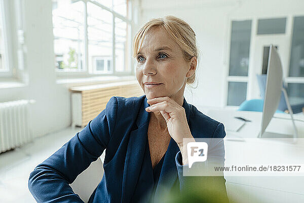 Thoughtful mature businesswoman with hand on chin at desk