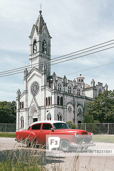 Cuba  Havana  Red vintage car parked in front of white painted church in La Vibora neighborhood