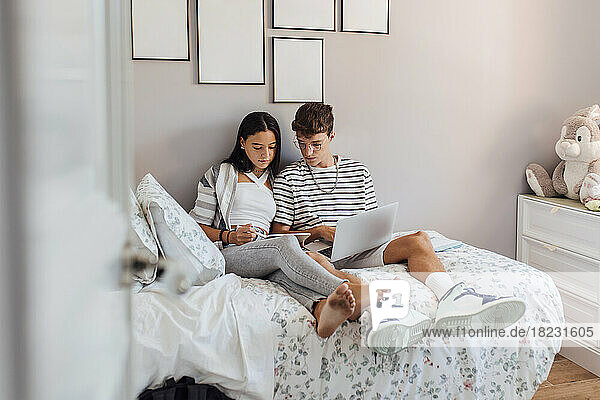 Siblings studying on tablet PC in bedroom at home