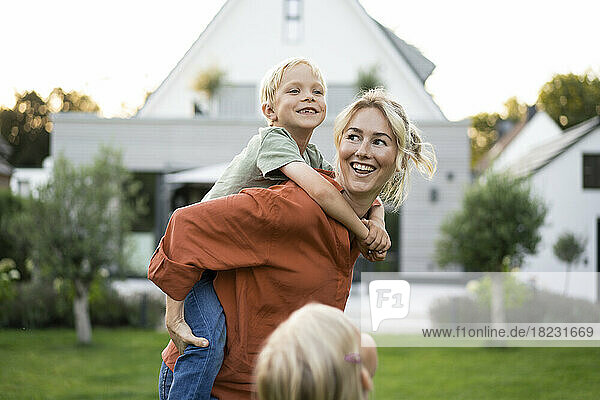 Happy mother giving piggyback ride to daughter in back yard