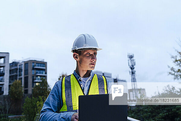 Contemplative engineer with laptop at dusk