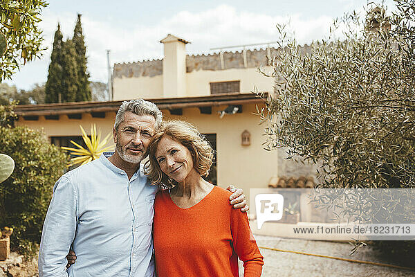 Happy mature couple standing in front of house