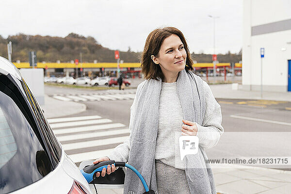 Thoughtful woman charging electric car at station