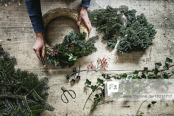 Hands of woman preparing Christmas wreath made of spruce  juniper  ivy  and rose hips