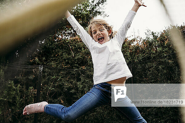 Playful girl with arms raised jumping in garden