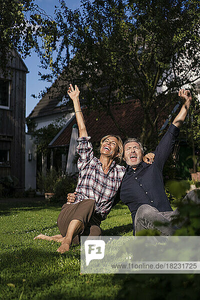 Cheerful man and woman with arms raised enjoying in back yard