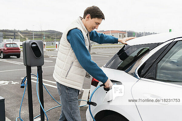 Man plugging charger in electric car at station