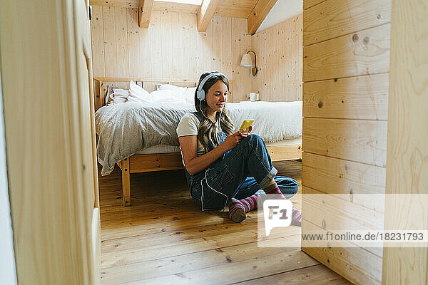 Smiling young woman using smart phone in bedroom
