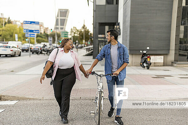 Happy woman and man walking with bicycle on road