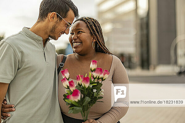 Happy young man embracing woman standing with bouquet of flowers