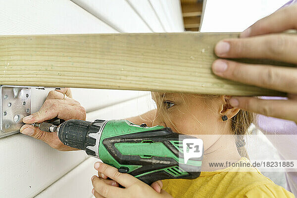 Girl installing bracket on wooden wall with father outside house