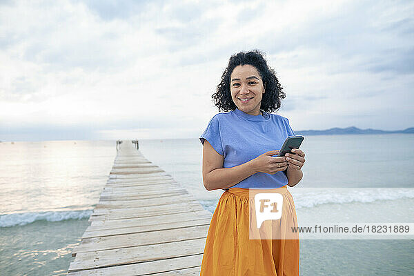 Happy woman standing with smart phone on jetty
