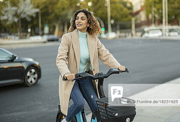 Smiling woman riding electric bicycle on footpath