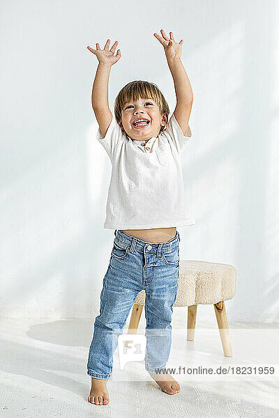 Boy with arms raised standing in front of wall at home