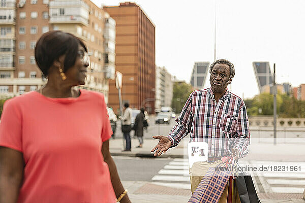Mann hält Einkaufstüten und spricht mit Frau  die die Straße überquert