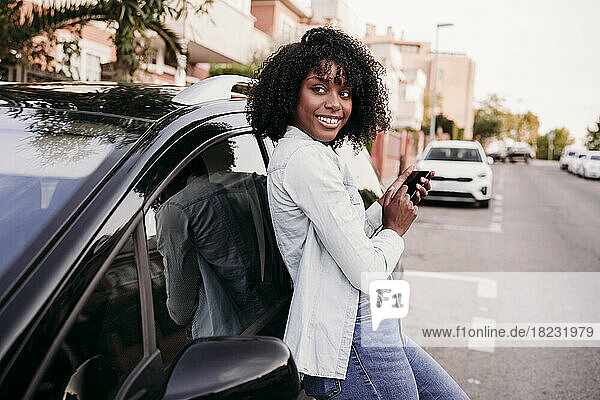 Contemplative woman with smart phone leaning on car