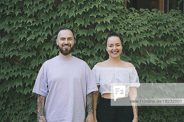 Happy hipster couple standing in front of green ivy plants