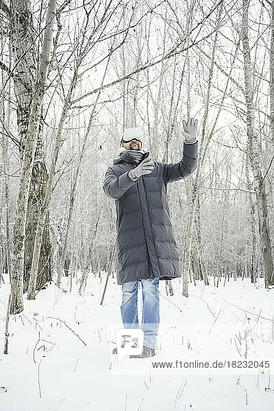 Man wearing virtual reality simulator standing on snow gesturing amidst bare trees