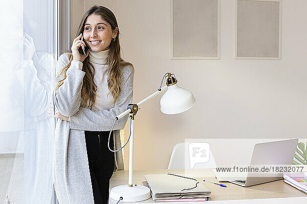 Happy young woman talking on mobile phone at home