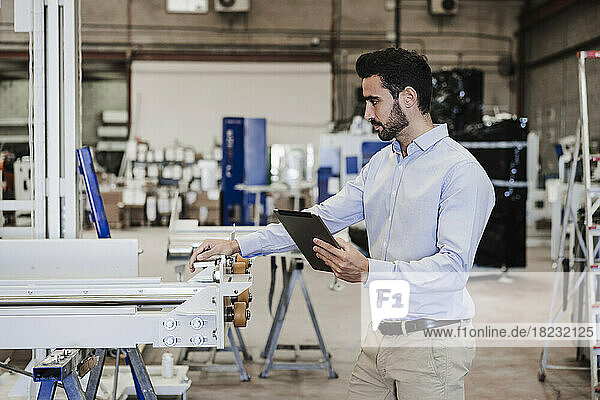 Businessman with tablet PC operating machine in industry