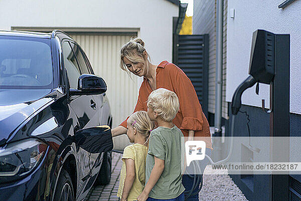 Woman charging electric car in front of children