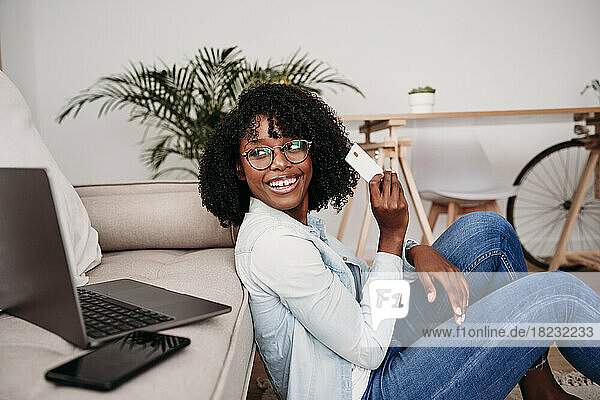 Happy businesswoman with credit card looking at laptop on sofa