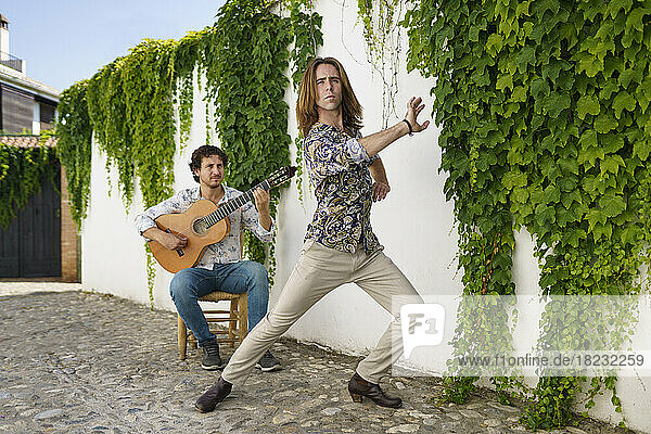 Dancer performing flamenco with guitarist by wall