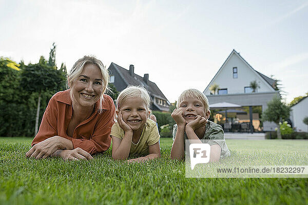Smiling woman with children leaning on elbows in back yard