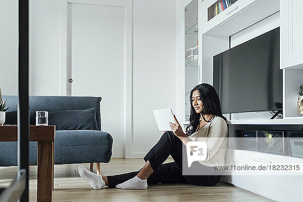 Junge Frau lernt mit Tablet-PC und sitzt zu Hause auf dem Boden